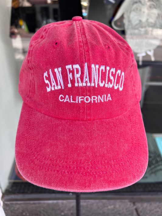 Front-facing view of a vibrant red washed cotton baseball cap featuring the words 'San Francisco' in a bold white arched font with 'California' embroidered underneath.