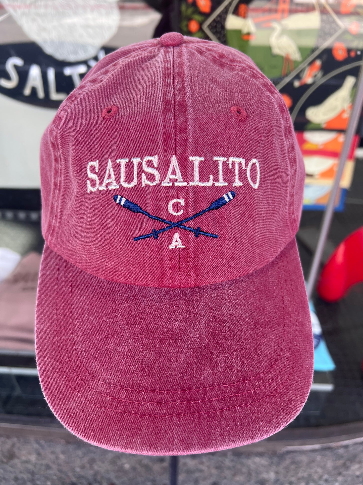 Brick red washed cotton cap featuring embroidered "SAUSALITO CA" text and crossed navy blue rowing oars.