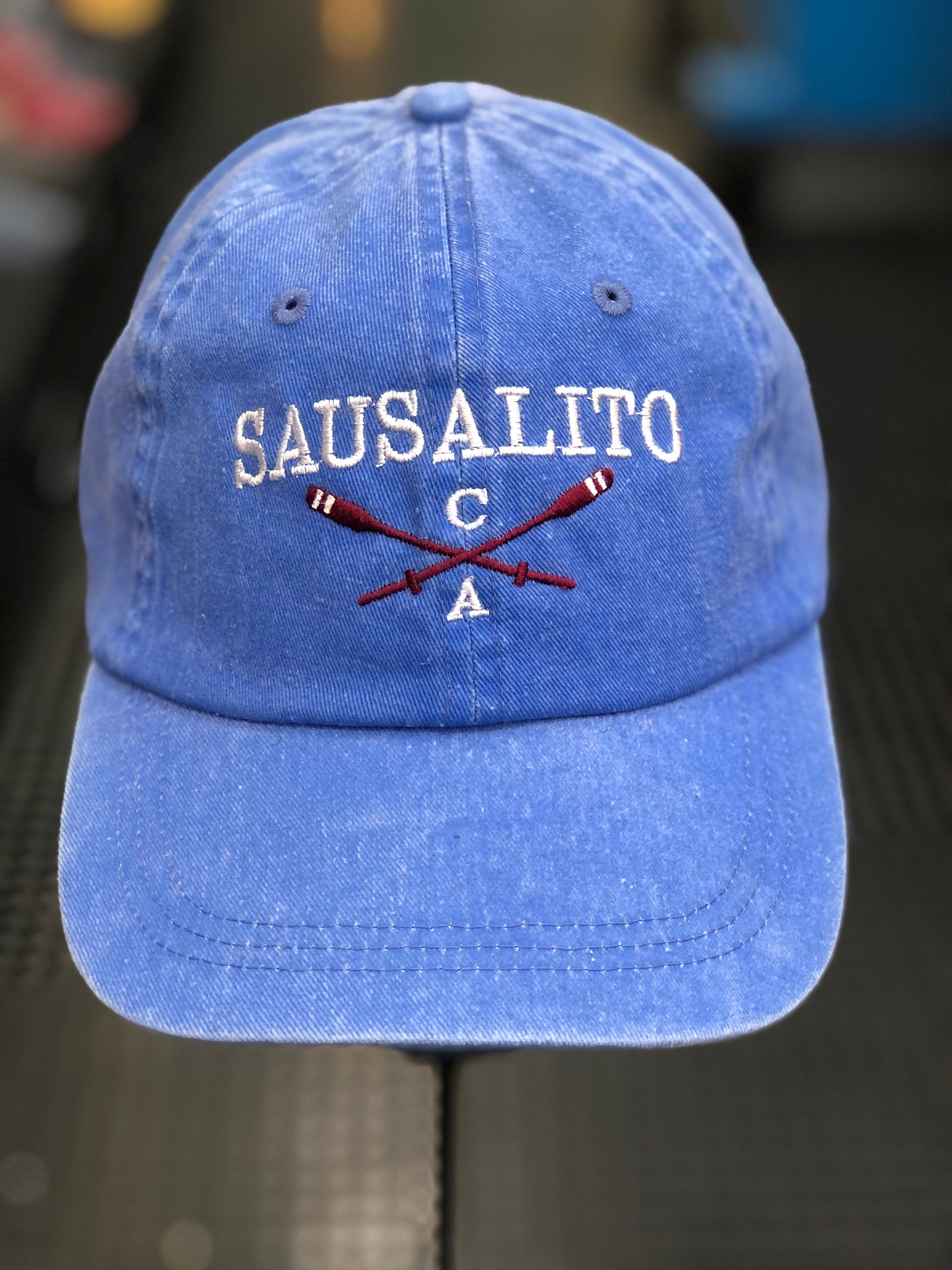Washed denim cotton cap with embroidered "SAUSALITO CA" text and crossed rowing oars, representing San Francisco Bay's rowing heritage.