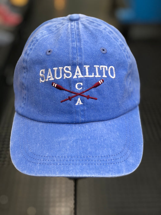 Washed denim cotton cap with embroidered "SAUSALITO CA" text and crossed rowing oars, representing San Francisco Bay's rowing heritage.
