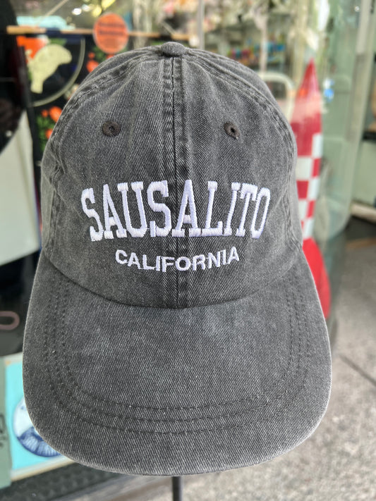 A close-up front view of the charcoal-black over-washed cotton twill baseball cap, featuring arched white 'SAUSALITO' embroidery above 'CALIFORNIA', as seen in the product image.