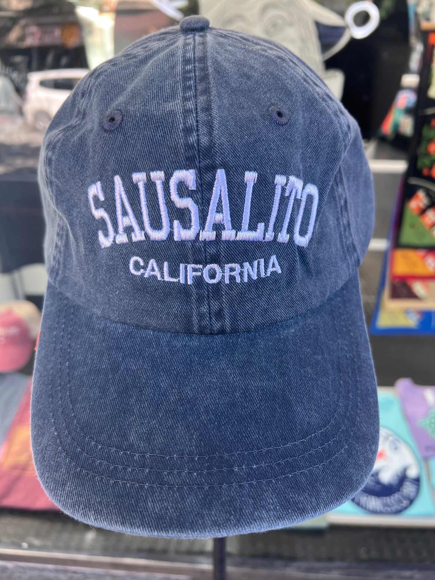 Front view of a navy blue washed cotton baseball cap featuring the words 'Sausalito' in a bold white arched font with 'California' embroidered directly underneath.