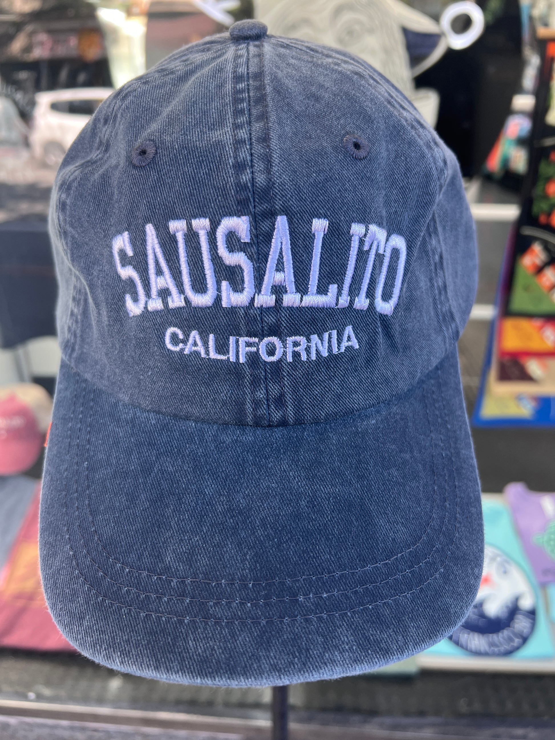 Front view of a navy blue washed cotton baseball cap featuring the words 'Sausalito' in a bold white arched font with 'California' embroidered directly underneath.