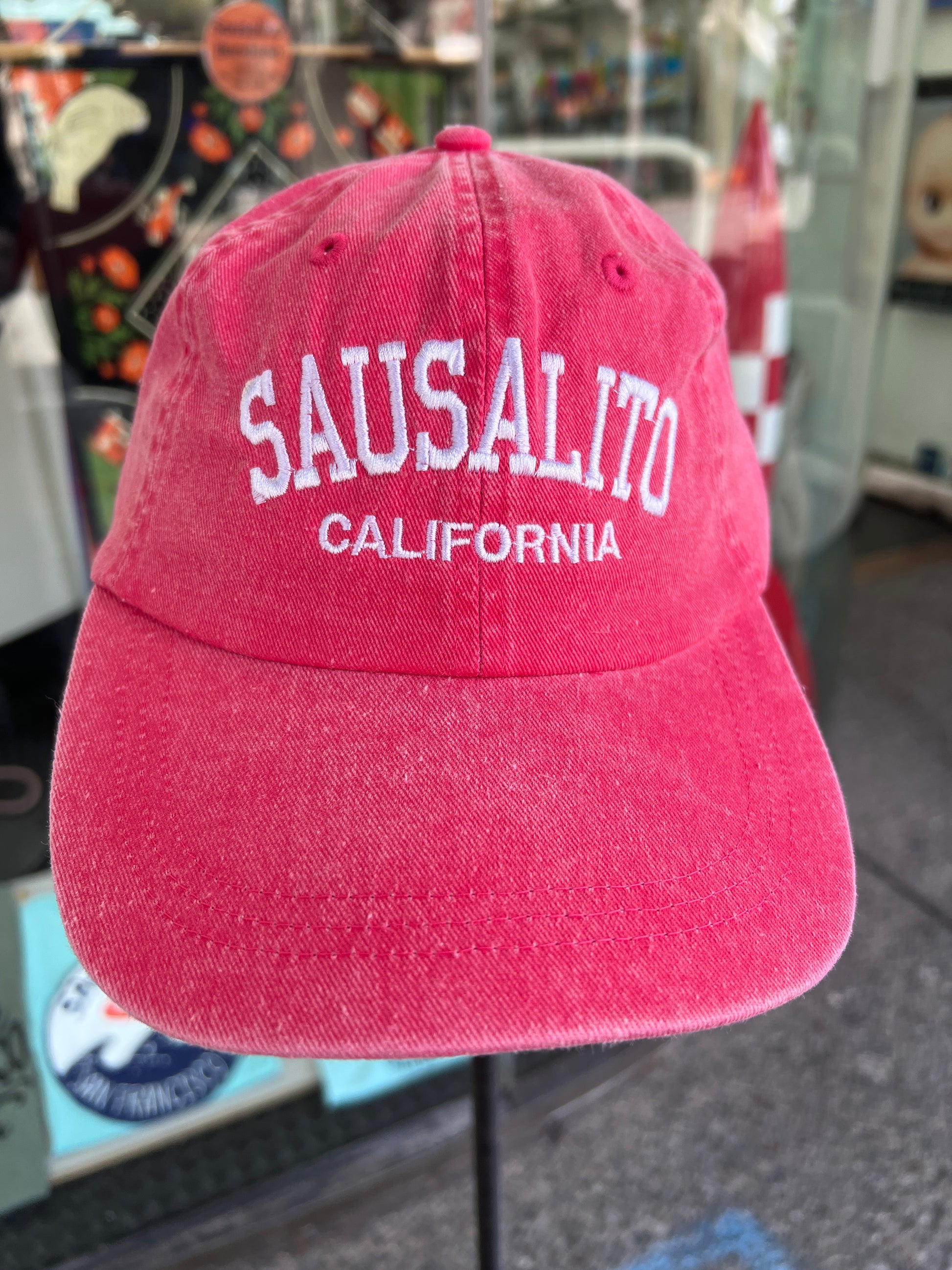 Front view of a vibrant pink washed cotton baseball cap featuring the words 'Sausalito' in a bold white arched font with 'California' embroidered directly underneath.