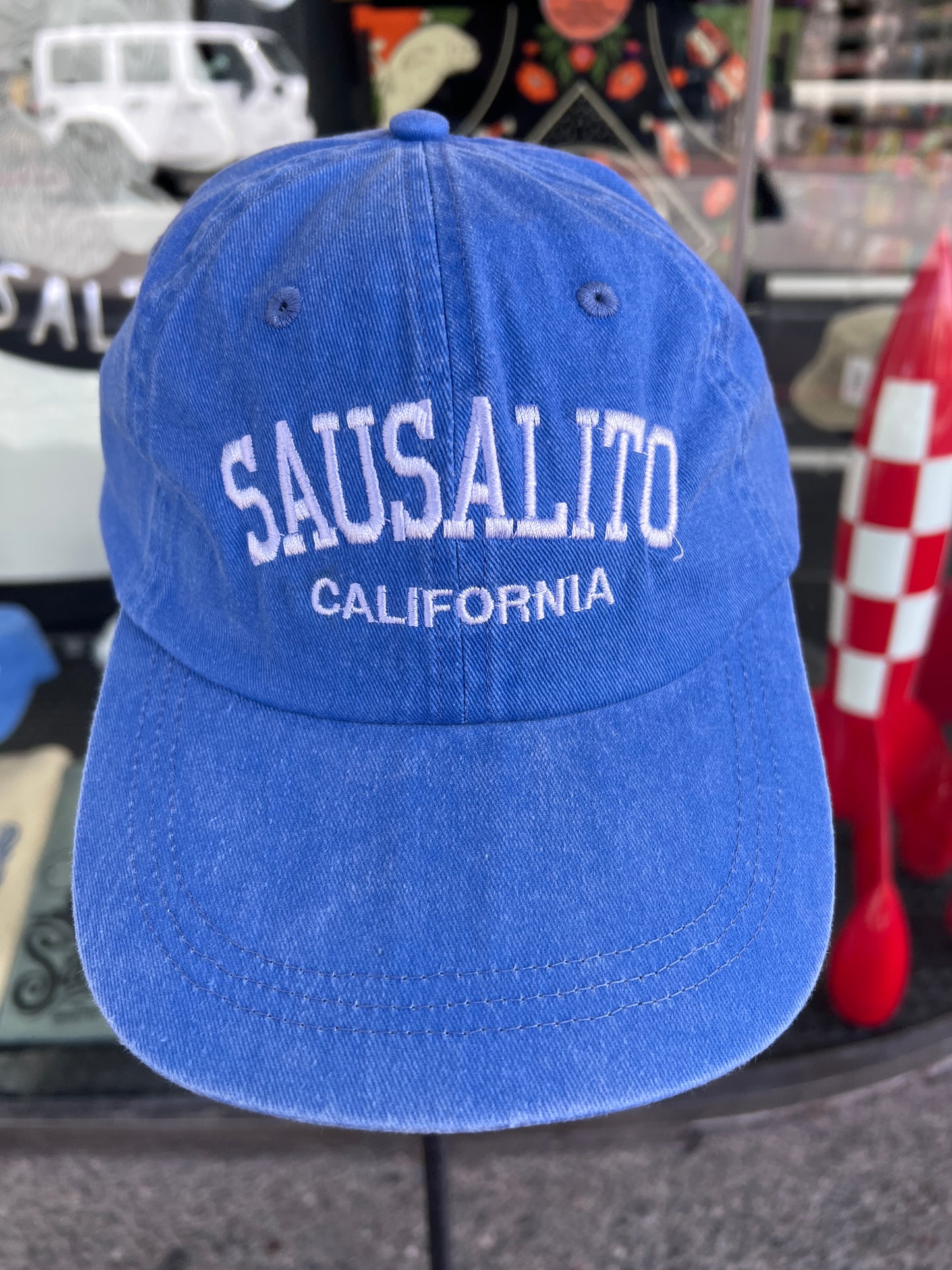 A close-up front view of the royal blue over-washed cotton twill baseball cap, featuring arched white 'SAUSALITO' embroidery above 'CALIFORNIA', as seen in the product image.