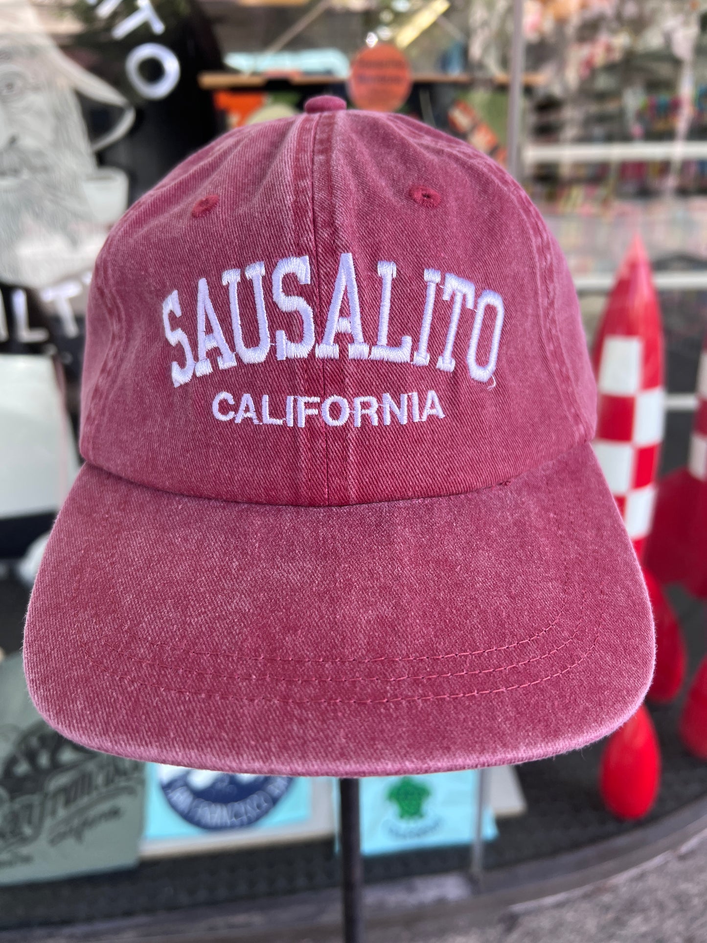 Front view of a wine-maroon washed cotton baseball cap featuring the words 'Sausalito' in a bold white arched font with 'California' embroidered directly underneath.