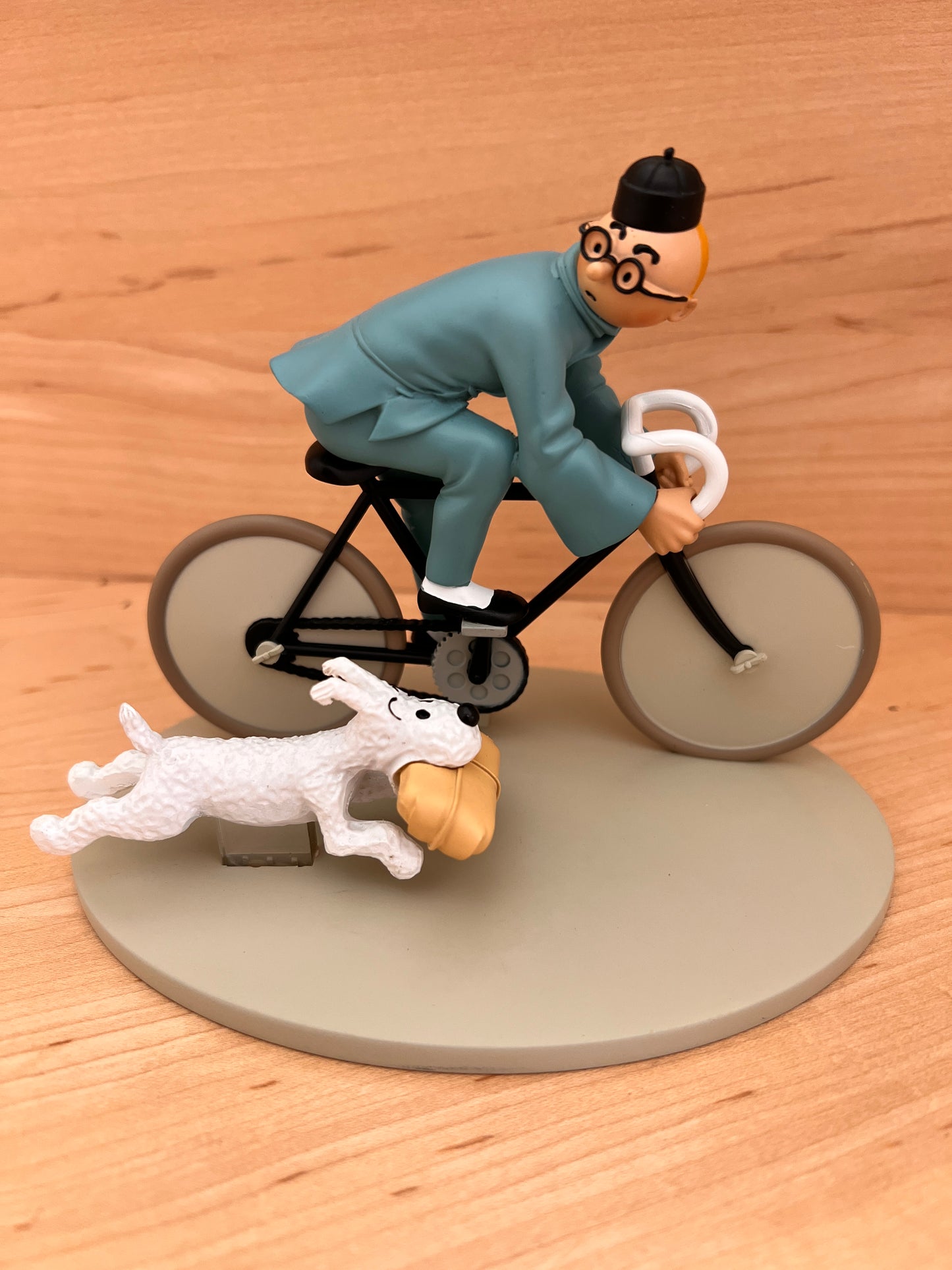 Hand-painted resin statuette of Tintin in a blue outfit riding a bicycle with Snowy running alongside carrying a package, from The Blue Lotus.