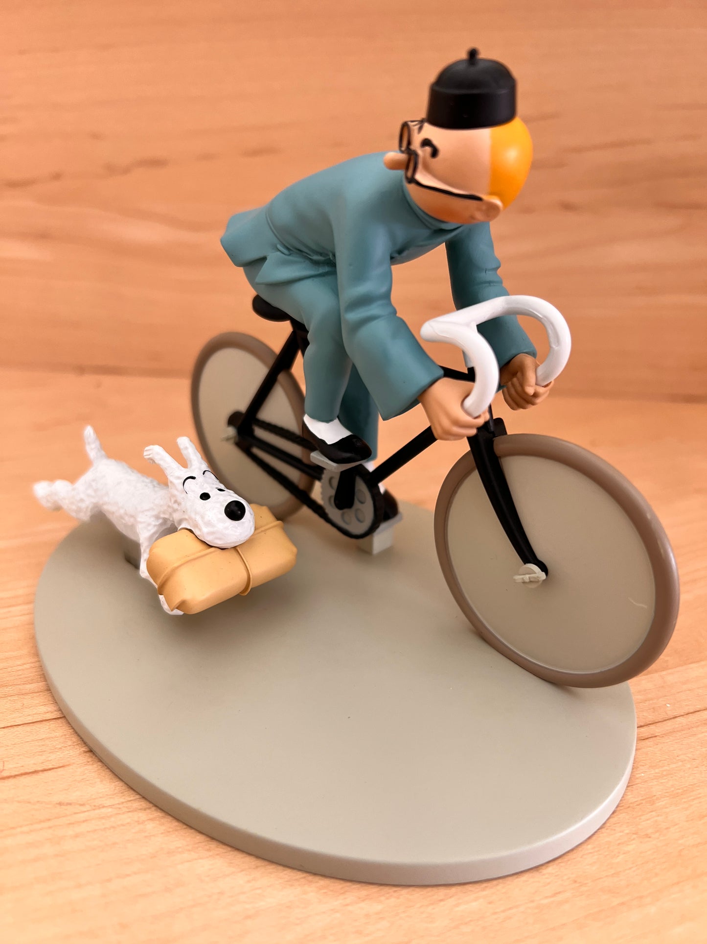 Side angle view of the hand-painted Tintin resin bicycle statuette from The Blue Lotus, showing Tintin leaning forward over the handlebars on a light grey base.