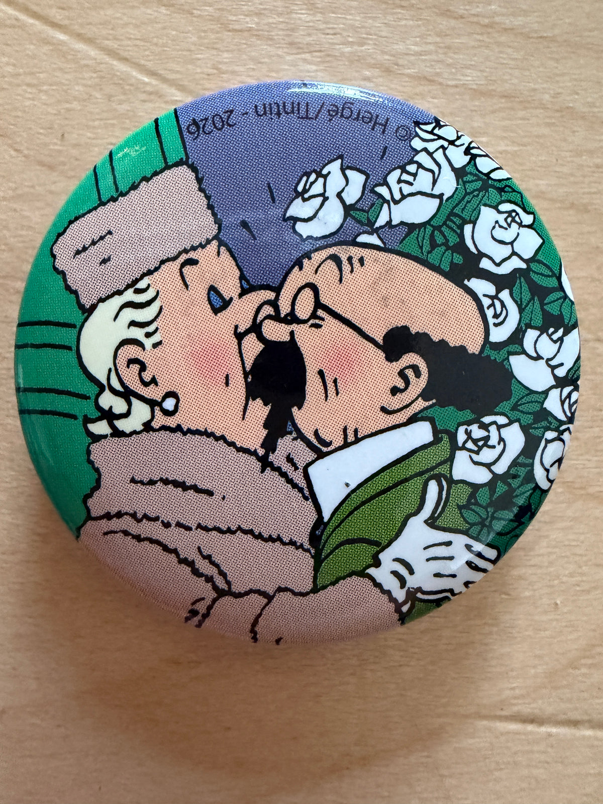 lose-up of a round 1-inch metal Tintin magnet featuring artwork from The Calculus Affair showing Professor Calculus and Bianca Castafiore greeting each other against a green background with white roses.
