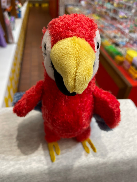 Colorful red parrot plush toy with yellow beak and blue wings, displayed in toy store, resembling Scarlet Macaw
