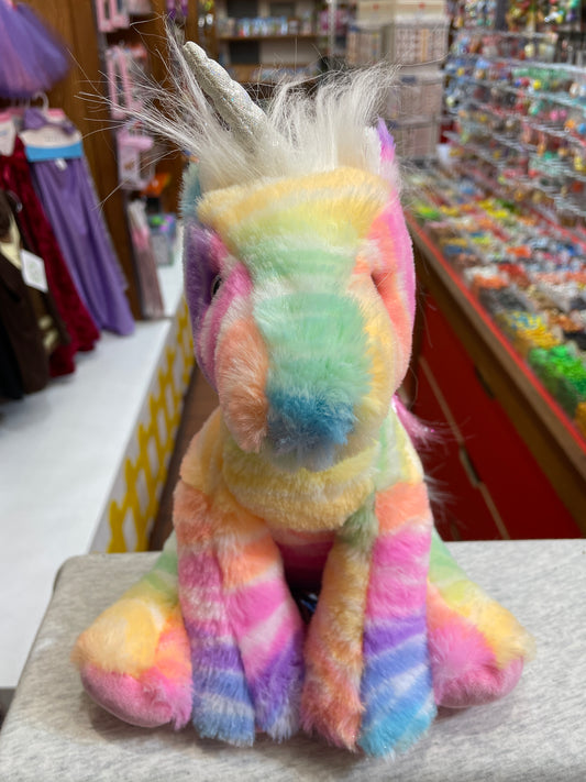 Colorful rainbow unicorn plush toy with glittery horn and fluffy mane, sitting on display in toy store aisle