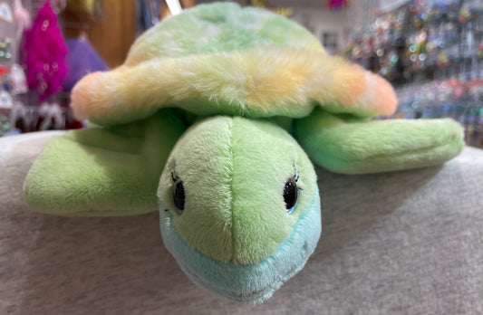 Colorful plush sea turtle Nyla with rainbow shell, green body, and sparkling blue eyes, perfect for cuddling and nautical adventures