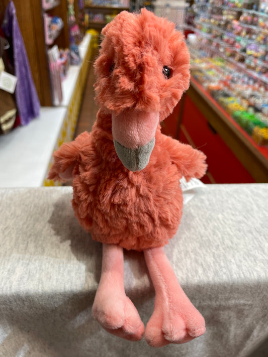 Soft, plush coral flamingo toy with long legs and beak, sitting on display in toy store aisle