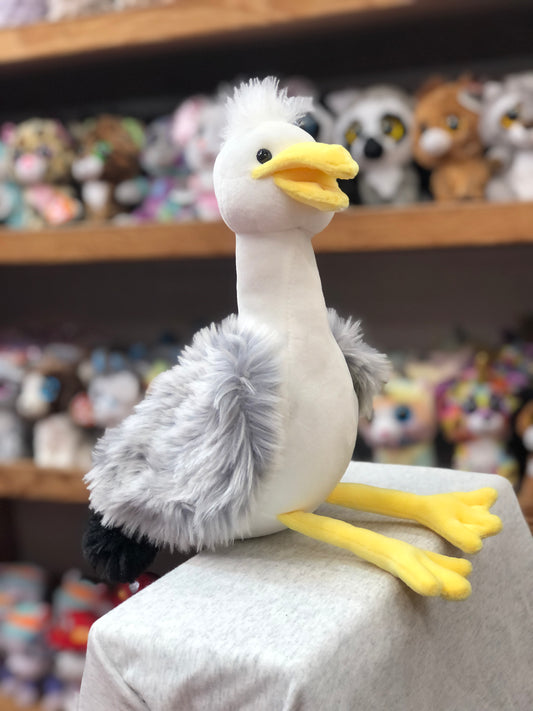 Cute plush seagull toy with white body, gray wings, yellow beak and feet, sitting on display with other stuffed animals