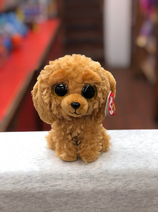 Ty Beanie Boo Noodles Goldendoodle plush toy with large sparkly eyes, golden fur, and Ty tag, sitting on a surface