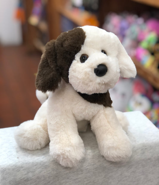 Adorable Douglas Donnie soft puppy plush toy with floppy ears, white and brown fur, sitting on display in a toy store