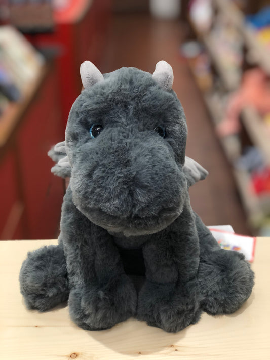 Cuddly gray dragon plush toy with bright blue eyes, small wings, and soft fur, sitting on wooden surface