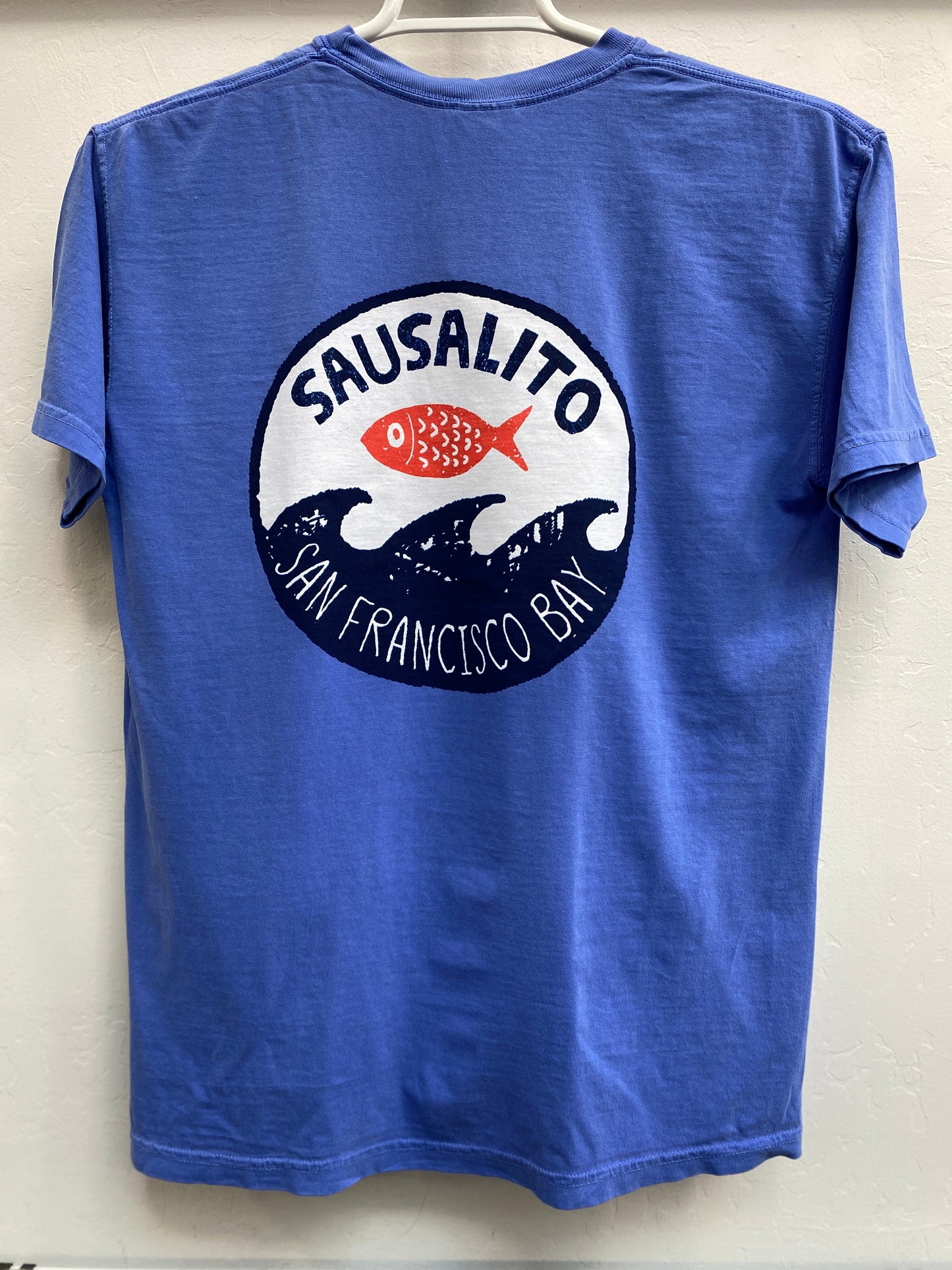Sausalito Fish Wave T-shirt design featuring a stylized red fish leaping above dark blue waves inside a circular San Francisco Bay logo on blue cotton fabric.