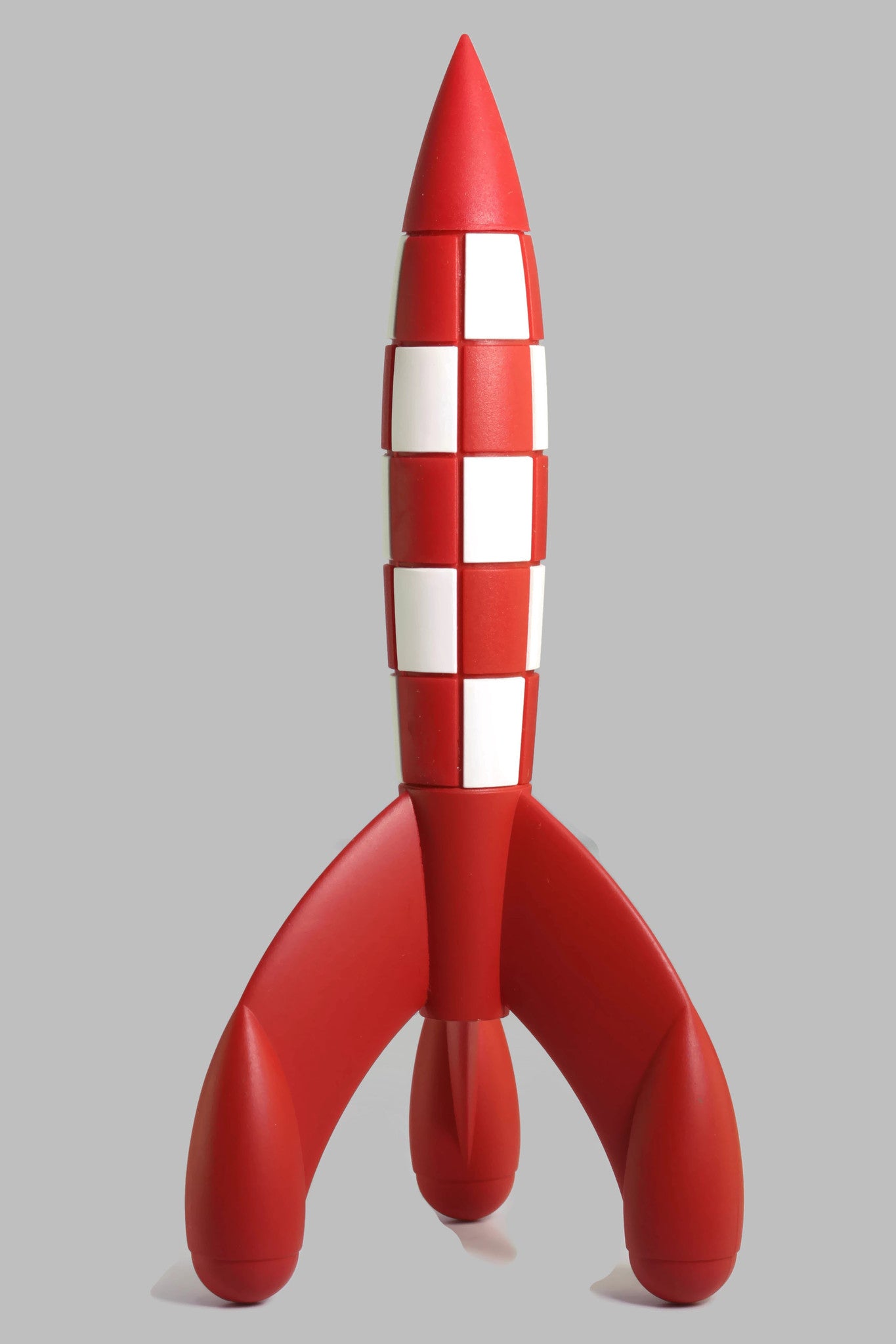 A model of the iconic red and white checkered moon rocket from The Adventures of Tintin, standing on its three curved base legs against a light gray background.