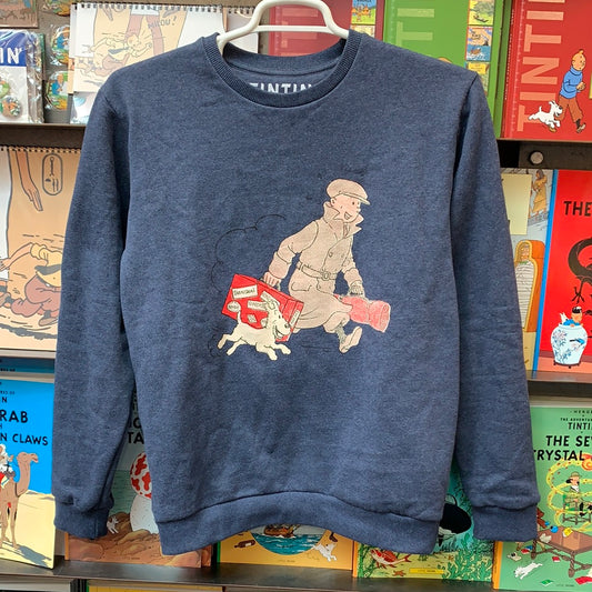 Navy blue unisex crewneck sweatshirt featuring classic Hergé comic art of Tintin in a trench coat and flat cap rushing home alongside Snowy, who is carrying a bright red suitcase covered in vintage Far East travel stickers, displayed in front of a background of Tintin comic books.