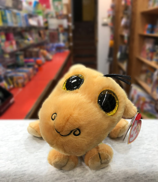 Ty Beanie Boo Jamal Camel plush toy with large sparkly eyes on display in a toy store, surrounded by colorful shelves