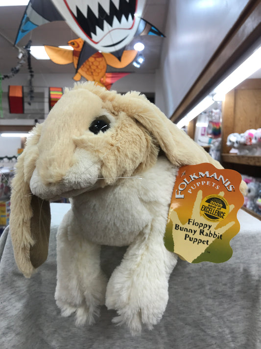 Folkmanis Floppy Bunny Rabbit puppet, cream-colored plush toy with long ears and award tag, displayed in toy store
