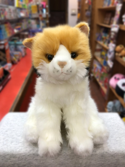 Adorable calico cat plush toy with golden and white fur, sitting on display in a toy store with colorful background