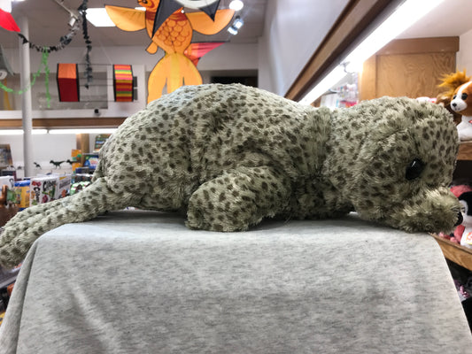 Realistic Folkmanis harbor seal puppet with spotted fur, lying on display in toy store surrounded by colorful decorations