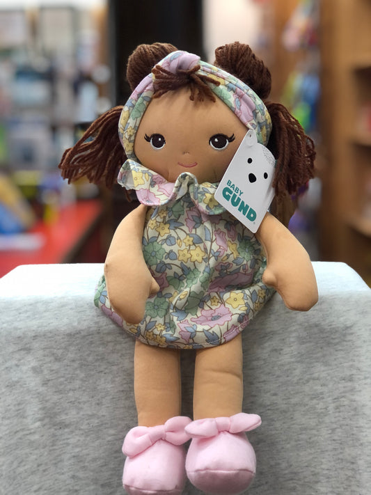Baby Gund toddler doll with floral dress, brown pigtails, and pink shoes, featuring embroidered face and brand tag