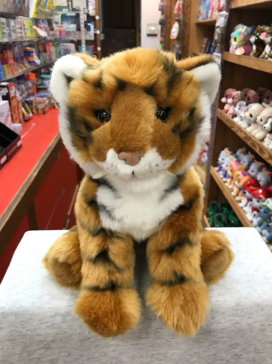 Adorable plush Bengal tiger cub with orange fur and black stripes, sitting in toy store display with expressive eyes and white accents