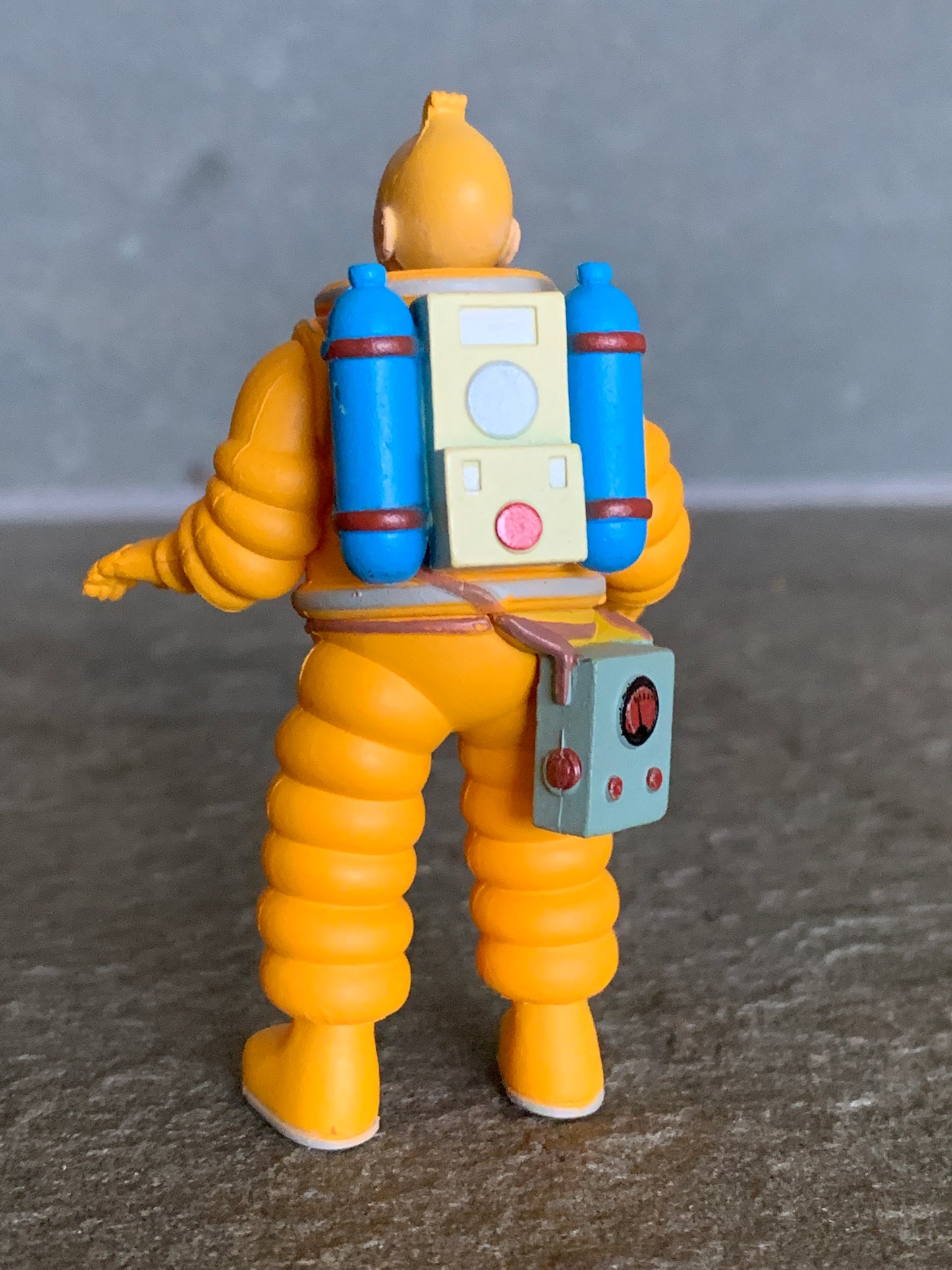 Rear view of the Tintin cosmonaut mini figure in a yellow spacesuit, showing a detailed white square backpack with blue oxygen tanks on either side and a control box hanging on his hip.